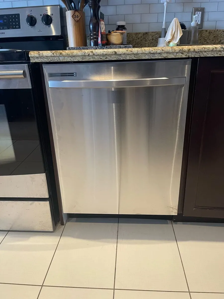 Stainless steel dishwasher installed under a granite counter beside a range